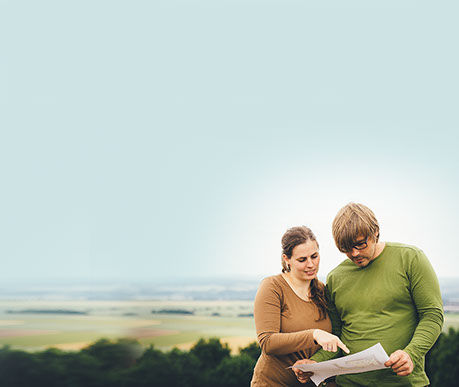 Marie und Nils Schneider stehen vor weitläufiger Landschaft und schauen gemeinsam in einen Plan.